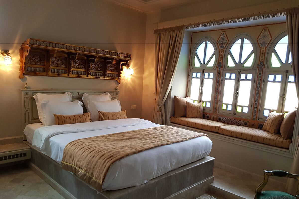 Un dormitorio con una cama grande, un banco junto a la ventana y paneles decorativos en la pared.
