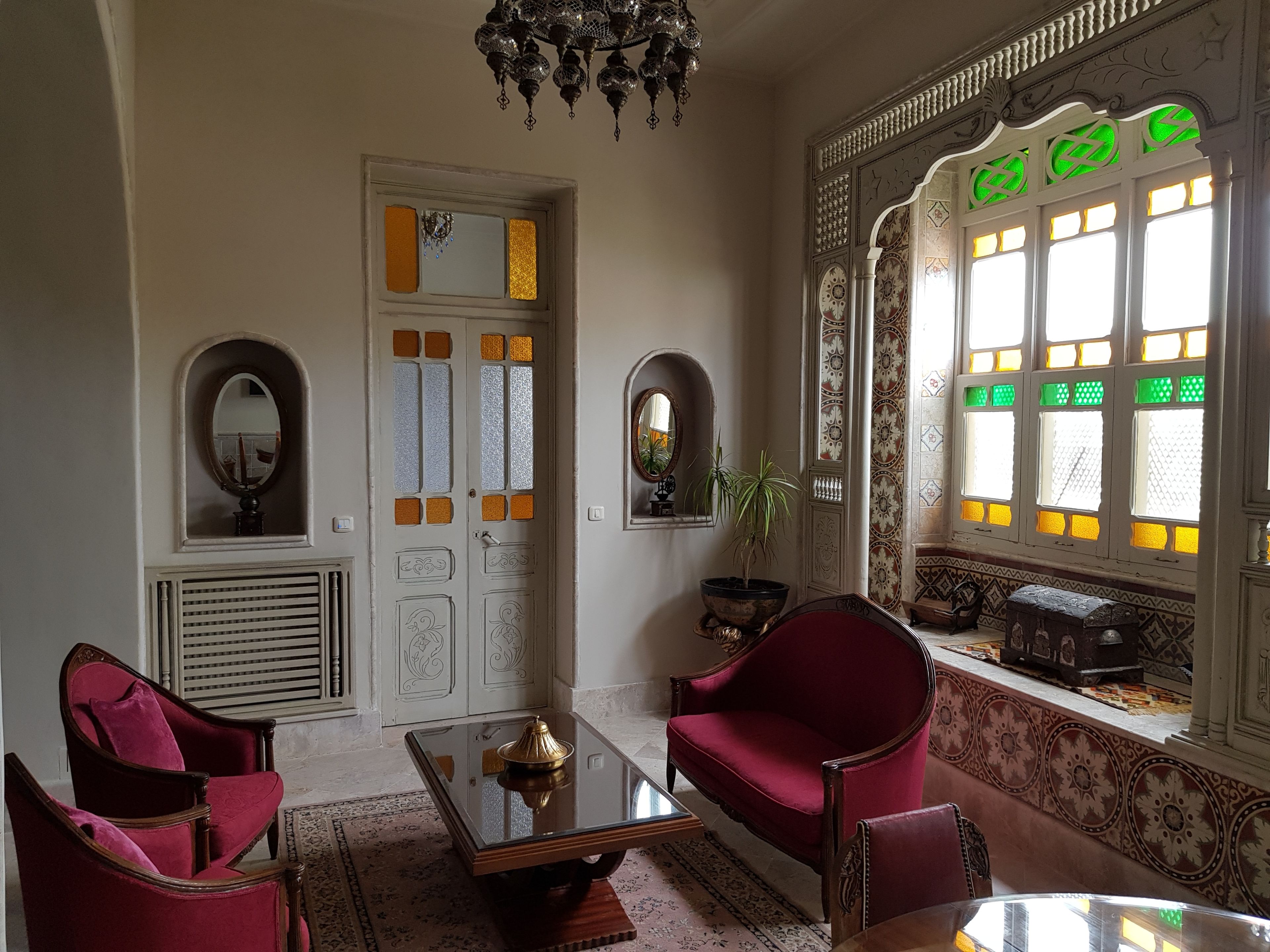A room with a traditional design, featuring a red armchair, a glass coffee table, and a chandelier.