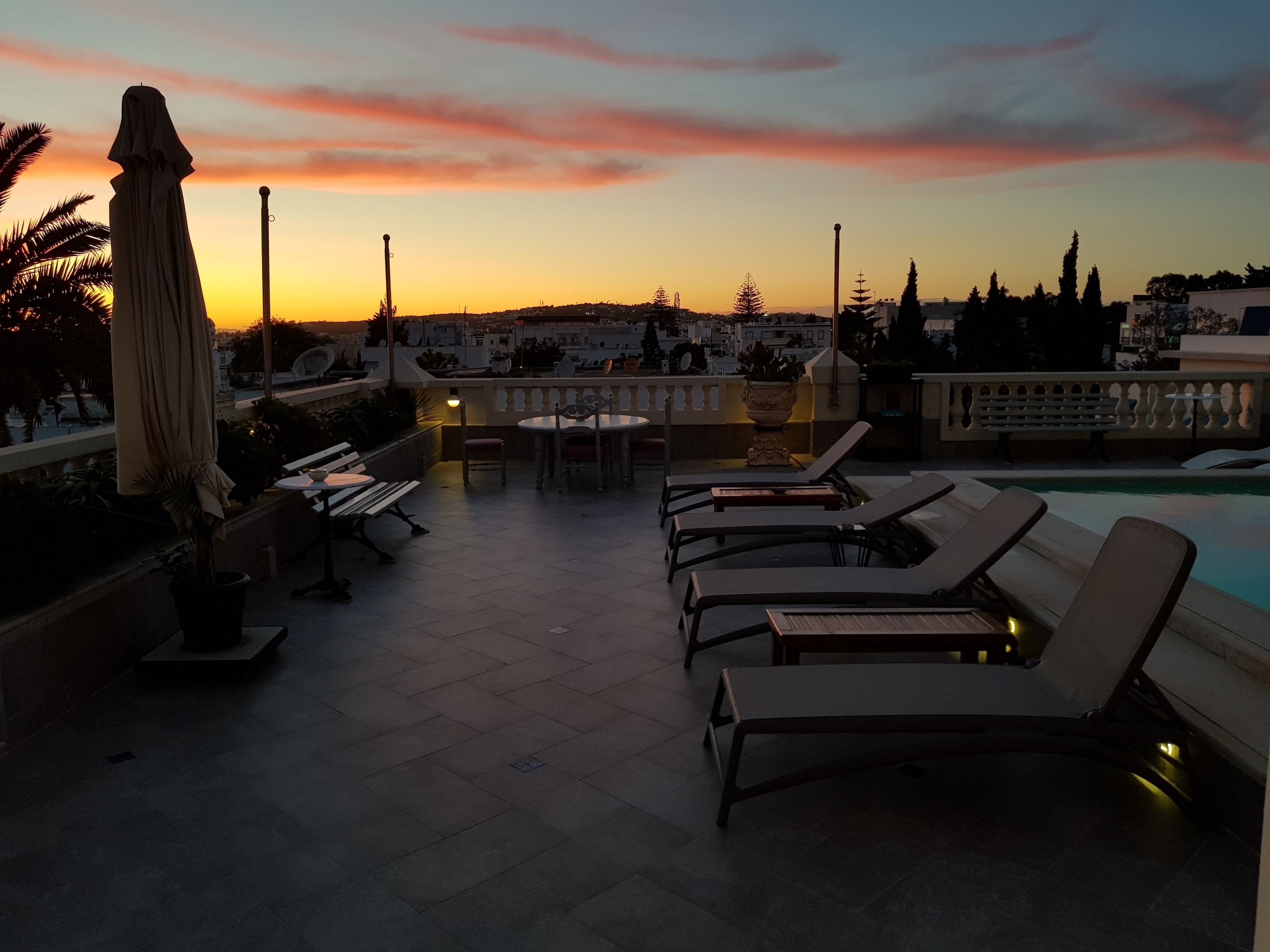 A rooftop terrace with lounge chairs, a table, and a pool.