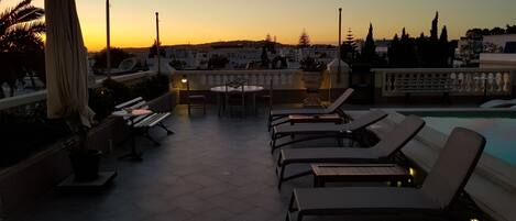 Una terraza en la azotea con sillones de descanso, una mesa y una piscina.