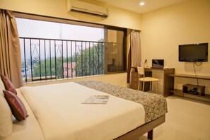A hotel room with a large bed, a desk with a chair, a television, and a balcony with a view of greenery. - Tim Grand Hotel (Mumbai)