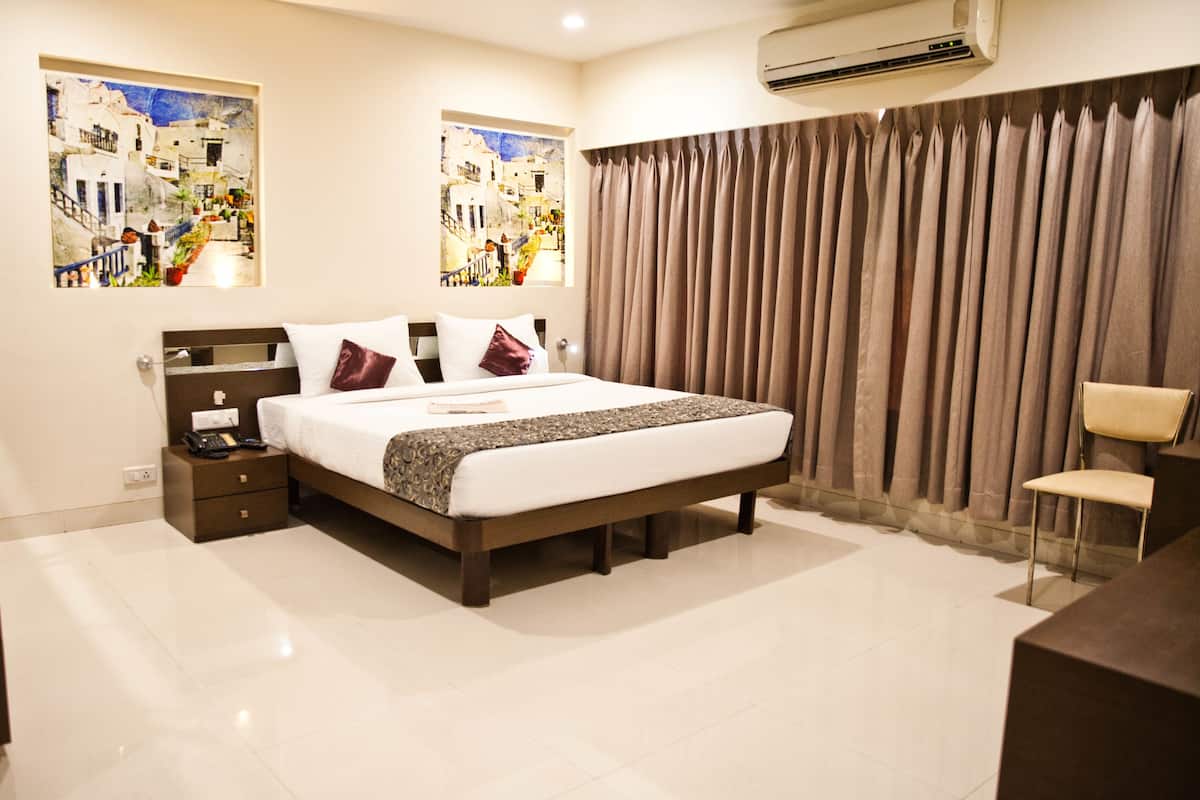 A modern hotel room with a large bed, a bedside table, a nightstand, a desk, and a chair.