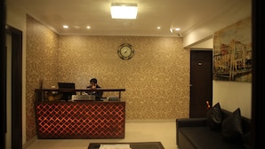 A reception area with a patterned wall, a clock, a reception desk, a sofa, and a painting. - Tim Grand Hotel (Mumbai)