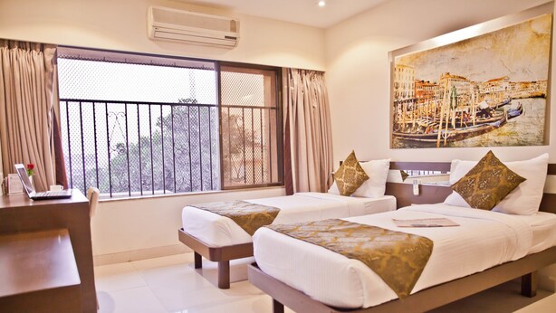 A hotel room with two beds, a desk, and a large window with curtains. - Tim Grand Hotel (Mumbai)