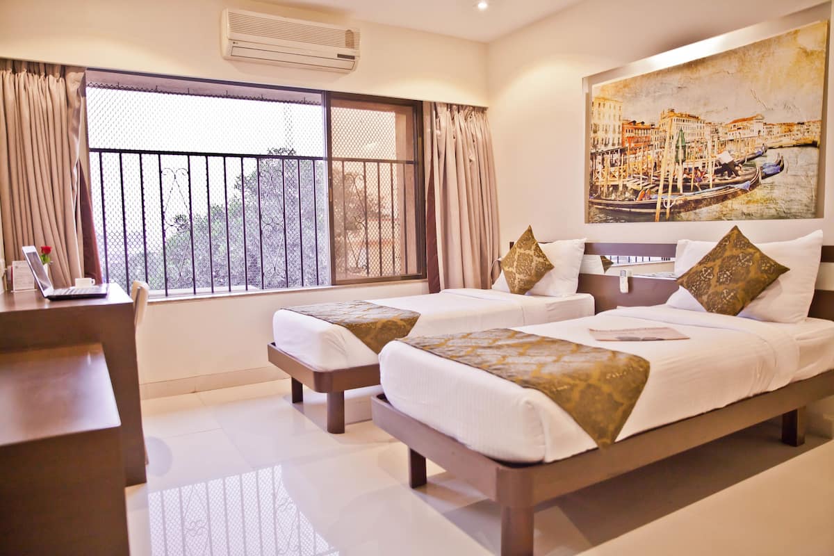 A hotel room with two beds, a desk, and a large window with curtains.