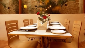 A dining table set with plates, a vase with red flowers, and chairs. - Tim Grand Hotel (Mumbai)