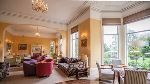 A spacious living room with a fireplace, comfortable seating, and large windows offering a view of the garden. - The Hotel Balmoral - Adults Only (Torquay)