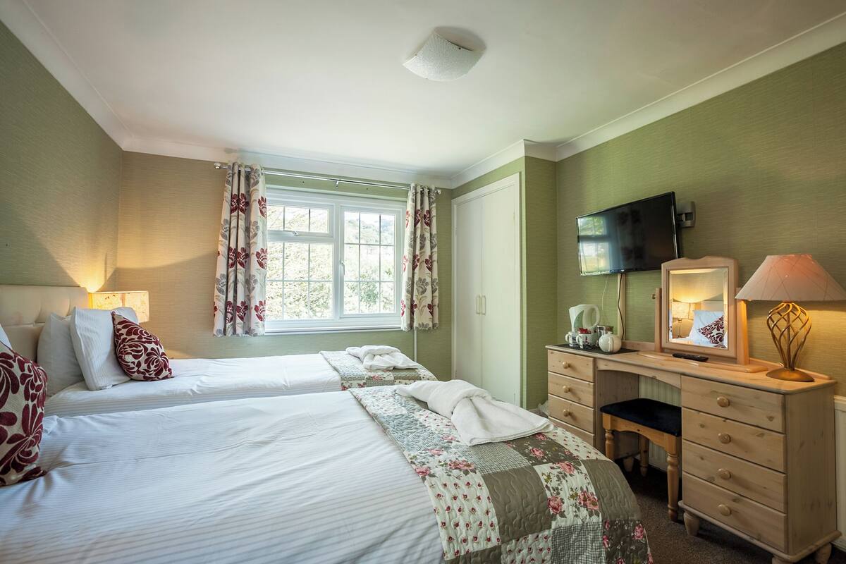 Quarto de hotel com duas camas, cômoda, televisão e janela com cortinas.