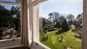 A view from a window overlooking a well-maintained garden with a fountain, benches, and a clear sky. - The Hotel Balmoral - Adults Only (Torquay)