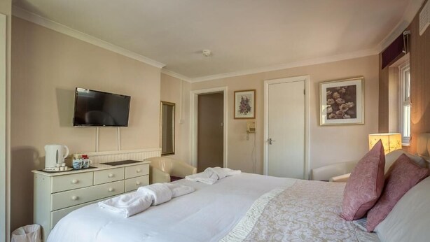 A hotel room with a large bed, a flat-screen TV mounted on the wall, a bedside table with a lamp, and a door leading to another room. - The Hotel Balmoral - Adults Only (Torquay)