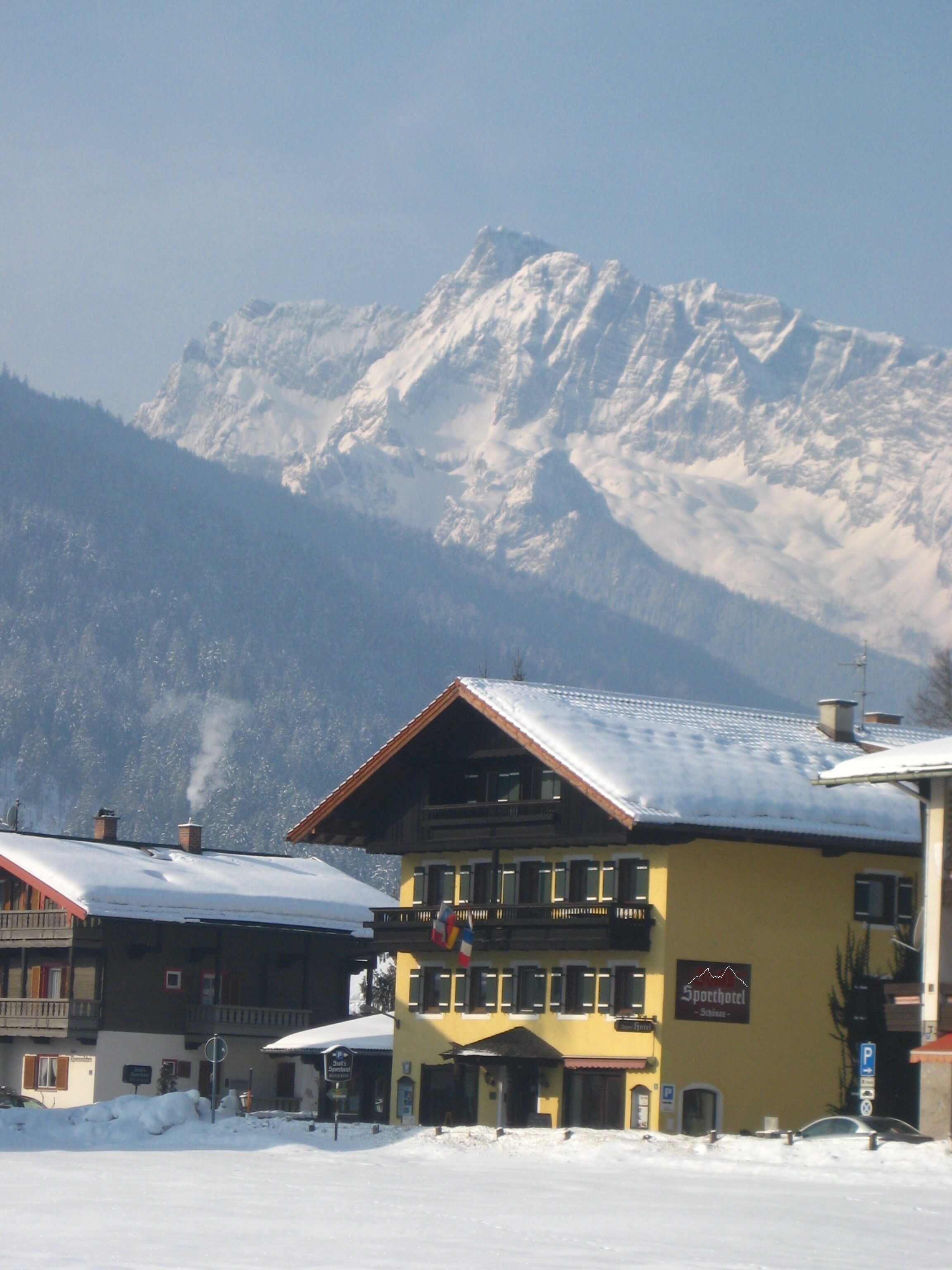 A hotel with a snow-covered roof, a balcony, and a mountain backdrop.