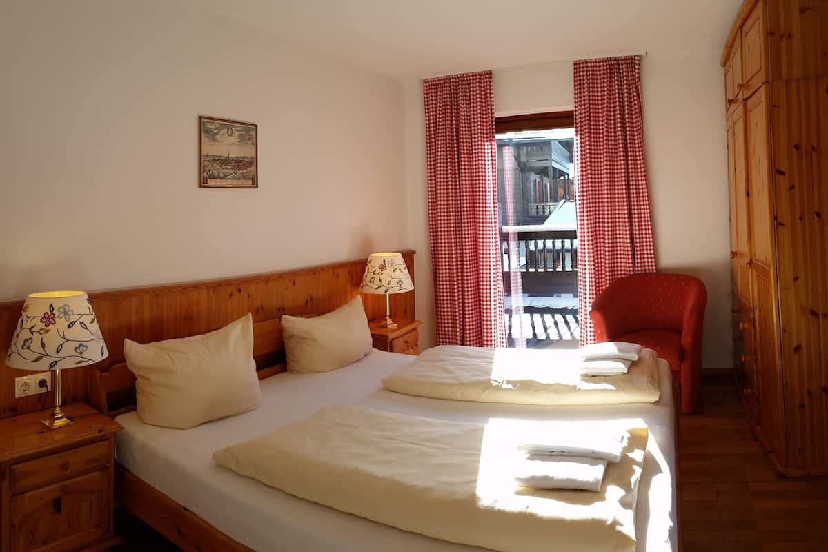 A bedroom with a wooden headboard, two bedside tables with lamps, a bed with white linens, a red chair, and a wooden wardrobe.