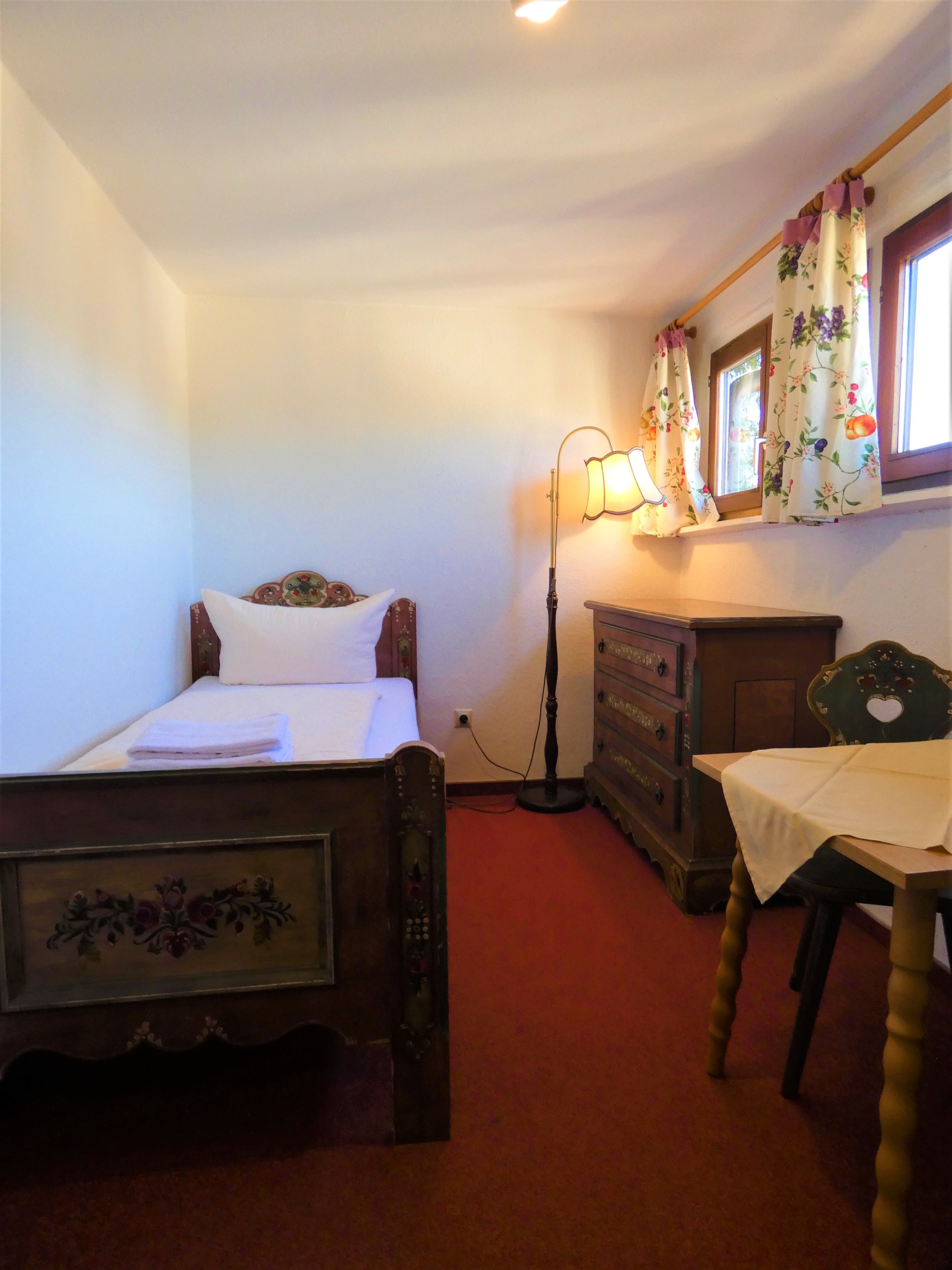 Un dormitorio con cama de madera, cómoda, silla, lámpara y ventana con cortinas florales.