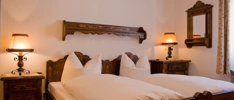 A double bed with white linens, two bedside tables with lamps, a wooden headboard, a mirror, and a floral curtain.