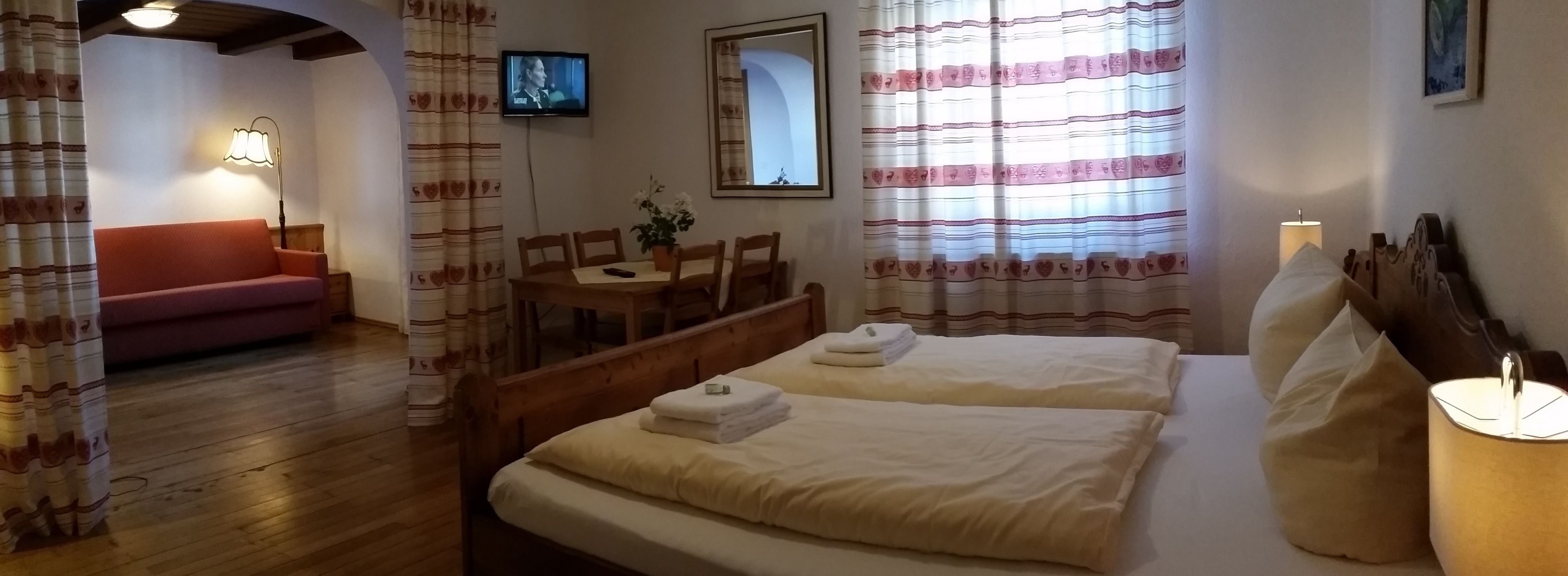 A hotel room with two beds, a sofa, a dining table with chairs, a TV, and a mirror.
