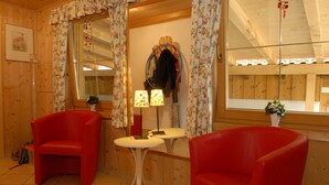 A cozy room with wooden walls, two red chairs, a small white table, and a mirror reflecting the room. - Hotel Pension Almrose (Wildschönau)