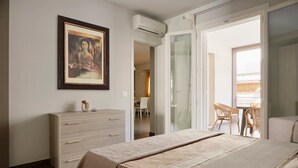 A bedroom with a bed, a dresser, a framed artwork, and a sliding glass door leading to a balcony with wicker furniture. - Casa Vacanza Talia CaseSicule- few meters from the beach (Pozzallo)