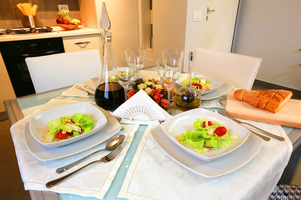 A dining table set with plates of salad, a loaf of bread, and wine glasses.