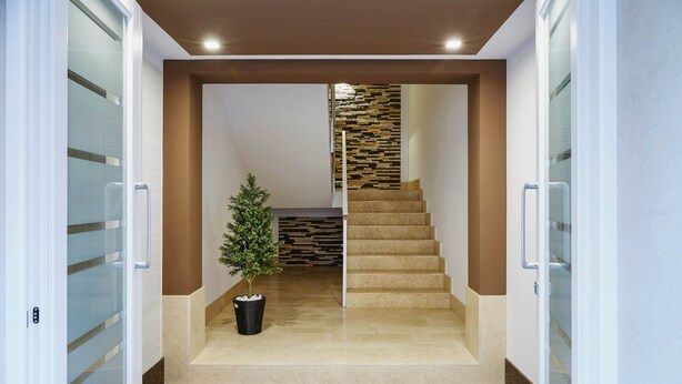 A modern interior with a stone-tiled floor, a staircase with a wooden accent wall, and a small potted plant. - Casa Vacanza Talia CaseSicule- few meters from the beach (Pozzallo)