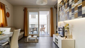 A modern living room with a sofa, dining table, TV, and a balcony with wicker chairs. - Casa Vacanza Talia CaseSicule- few meters from the beach (Pozzallo)