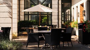 An outdoor patio with wicker furniture, a table, and an umbrella. - Hotel Gersfelder Hof (Gersfeld)
