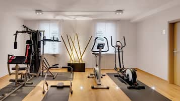 Een sportschool met diverse fitnessapparaten, waaronder een loopband, een hometrainer en krachtapparaten.