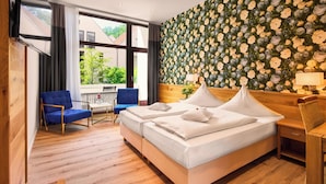 A hotel room with a large bed, a blue chair, a wooden desk, and a flower-patterned wall. - Hotel Gersfelder Hof (Gersfeld)