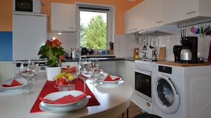 A modern kitchen with white cabinets, a built-in oven, and a washing machine. - pur NATUR & berlin ALEX 40min. (Steinhoefel)