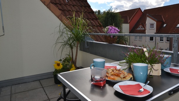 A balcony with a table set for two, featuring a blue mug, plates, napkins, and a small candle. - pur NATUR & berlin ALEX 40min. (Steinhoefel)