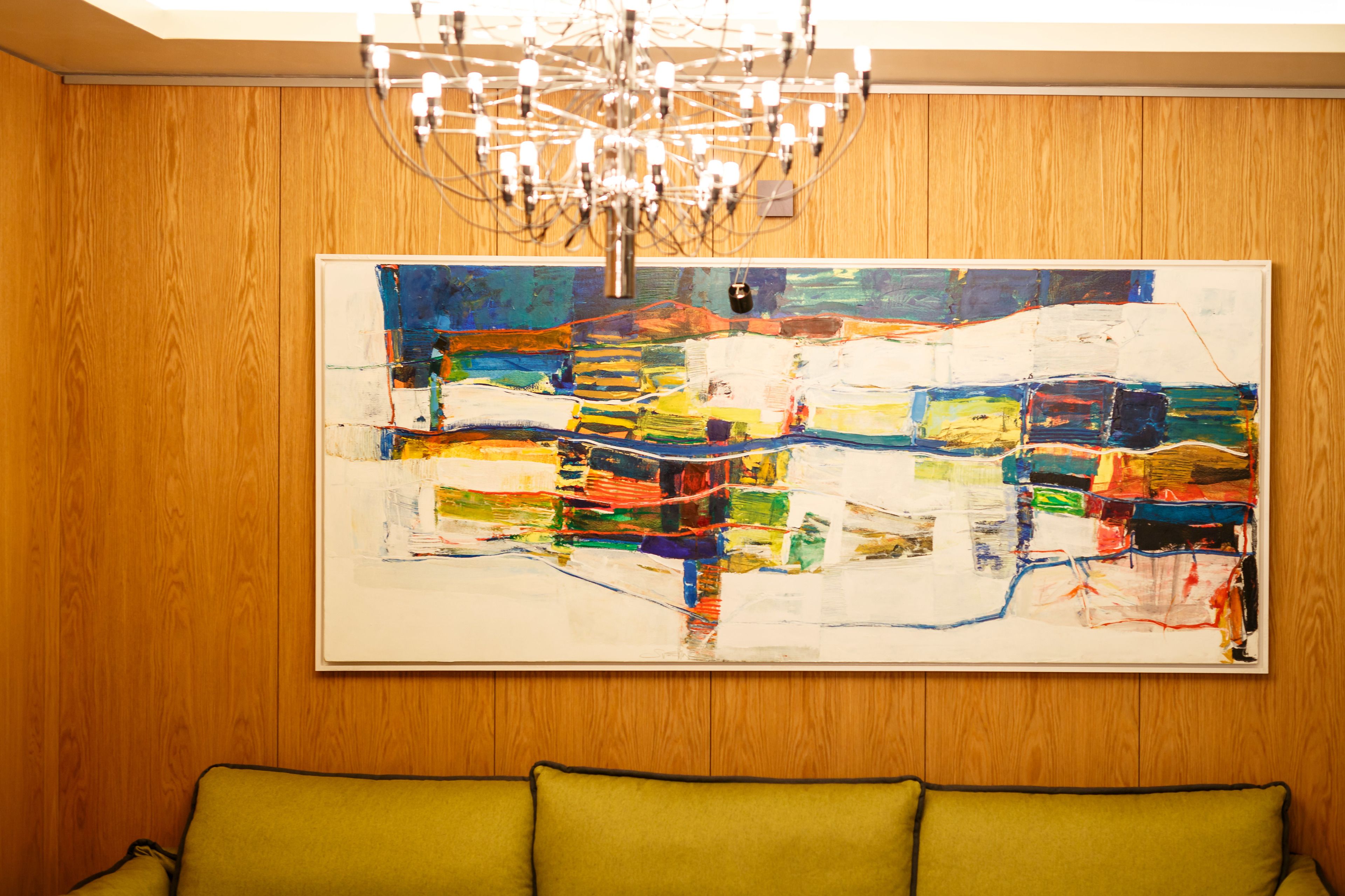 A room with a wooden paneled wall, a large abstract painting, and a green sofa.