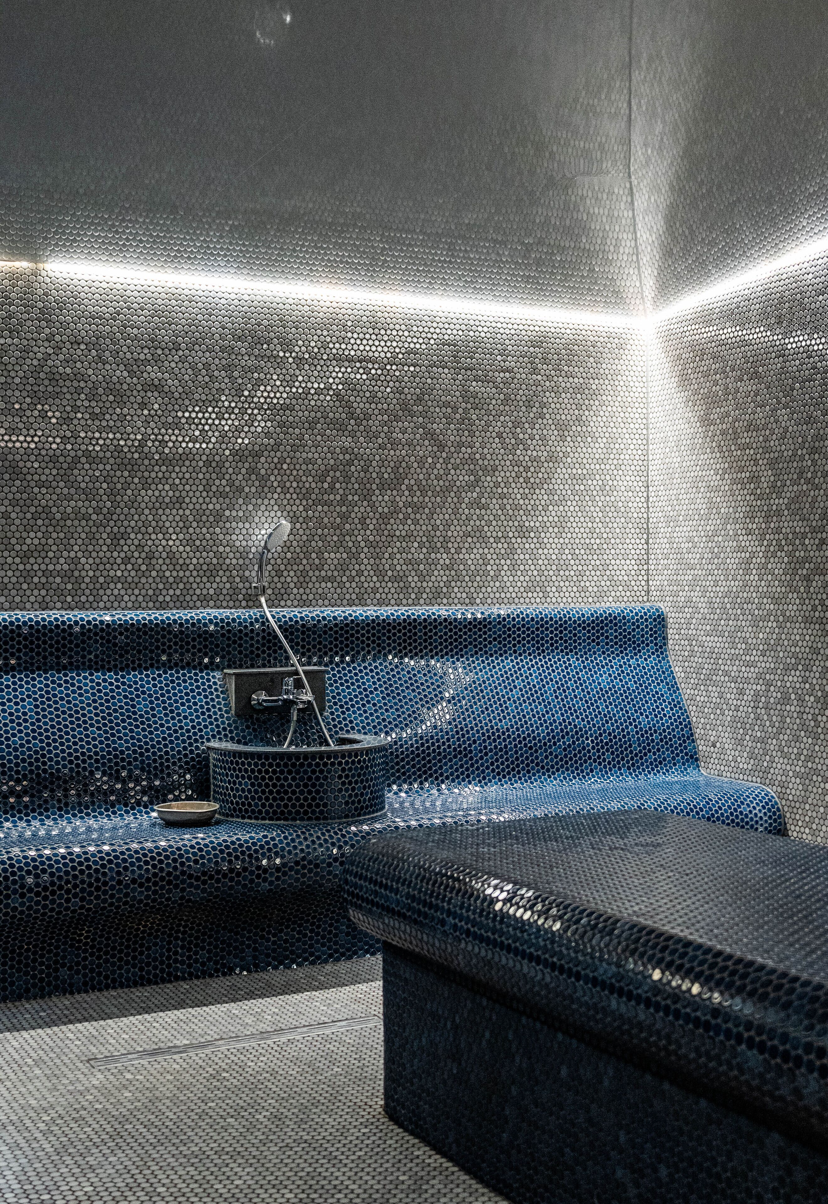 Un baño moderno con un banco azul con textura, un lavabo pequeño y una zona de ducha.