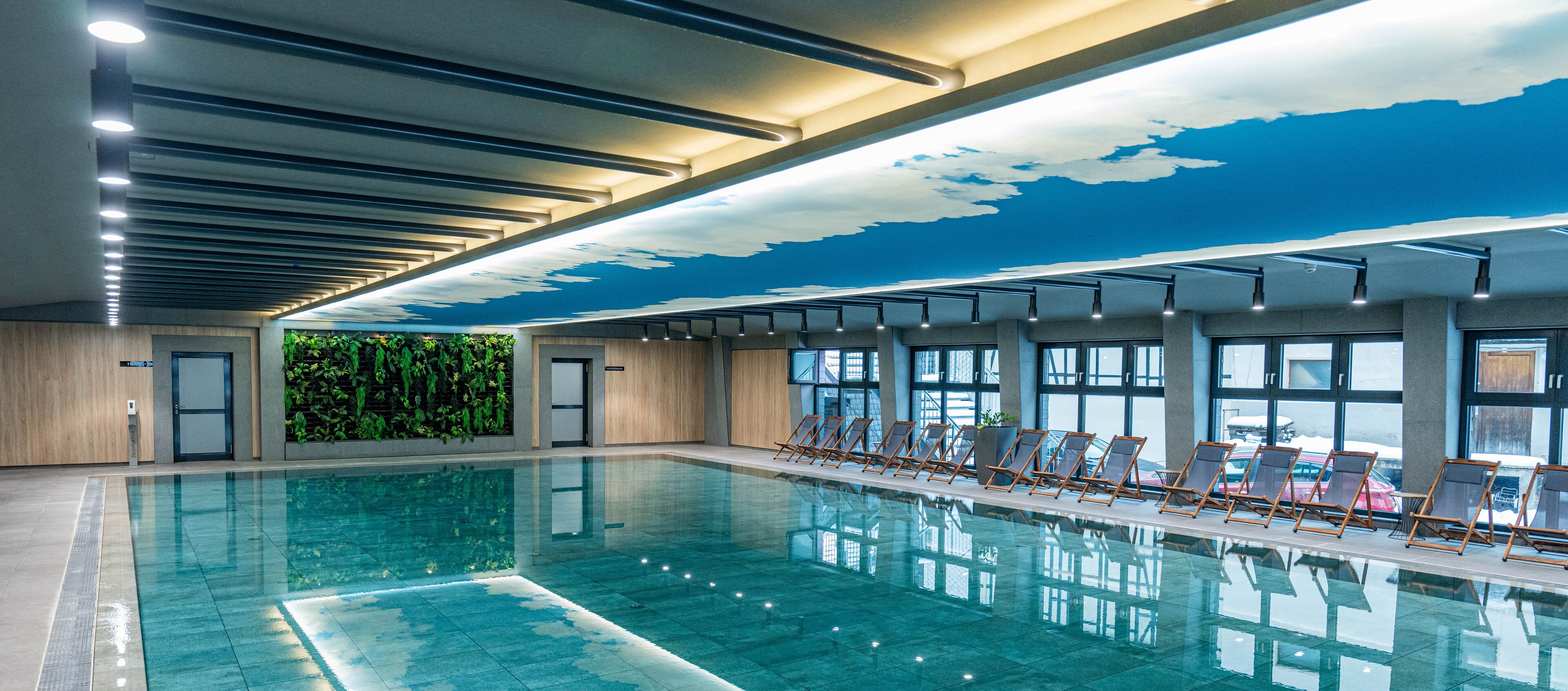 A swimming pool with clear water, surrounded by lounge chairs and a ceiling with a cloud design.