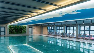 A swimming pool with clear water, surrounded by lounge chairs and a ceiling with a cloud design.