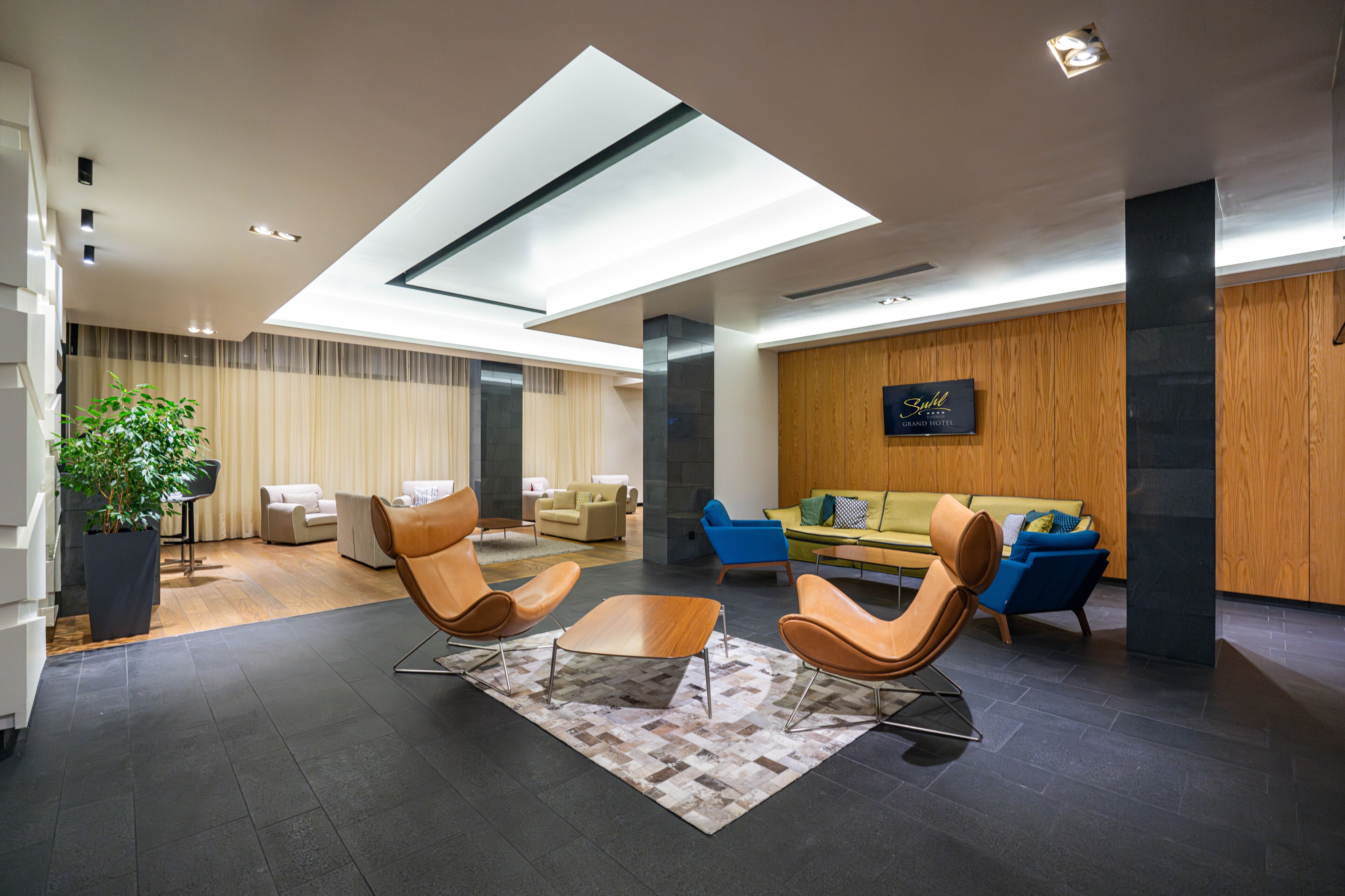A modern hotel lobby with a skylight, leather chairs, a sofa, and a potted plant.