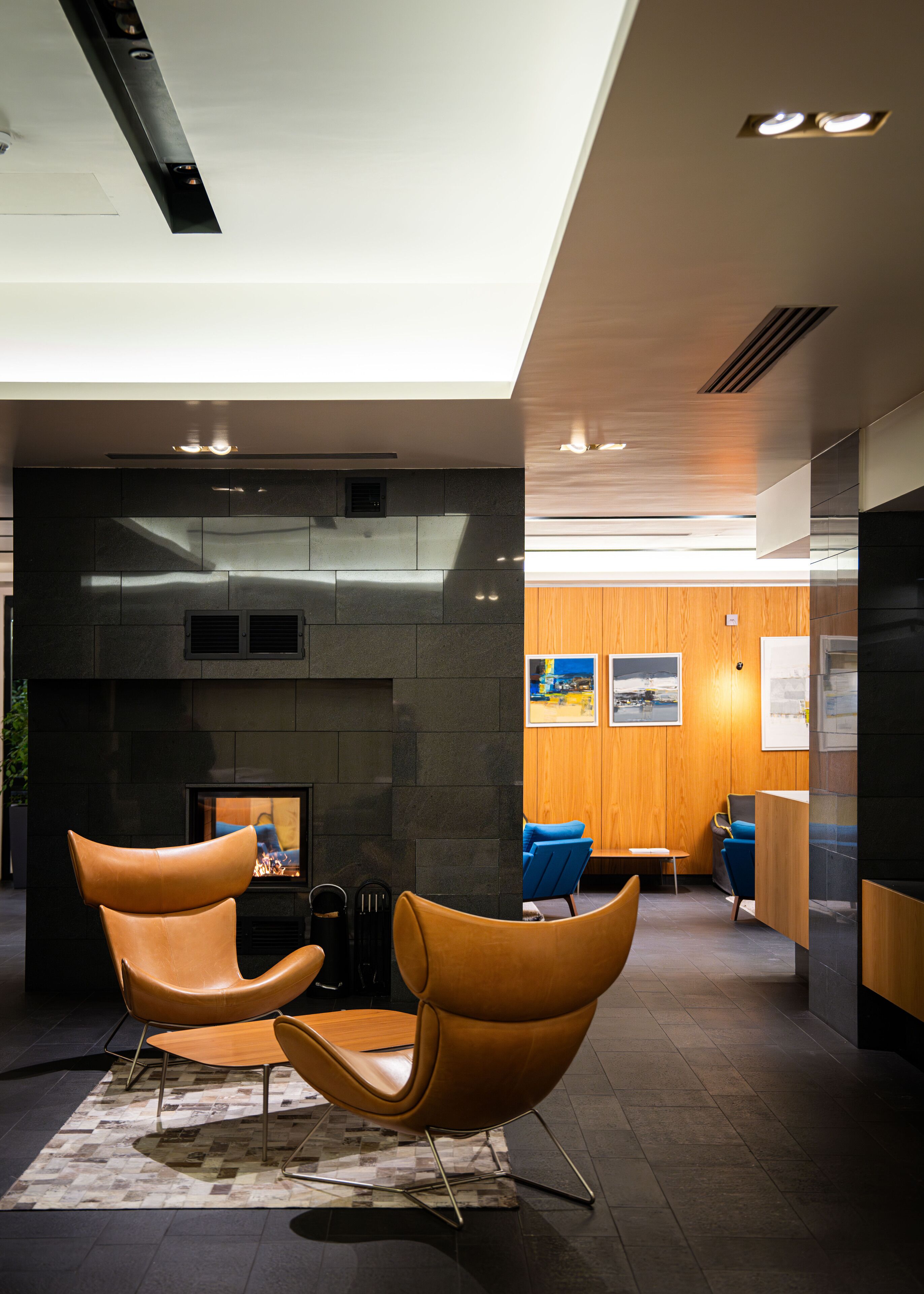A modern interior with a fireplace, leather chairs, and a wooden reception desk.