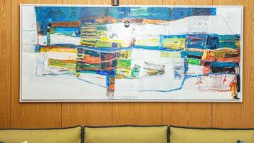 Un intérieur moderne agrémenté d’un grand tableau abstrait, d’un lustre original et d’un canapé de couleur moutarde orné de coussins à motifs.