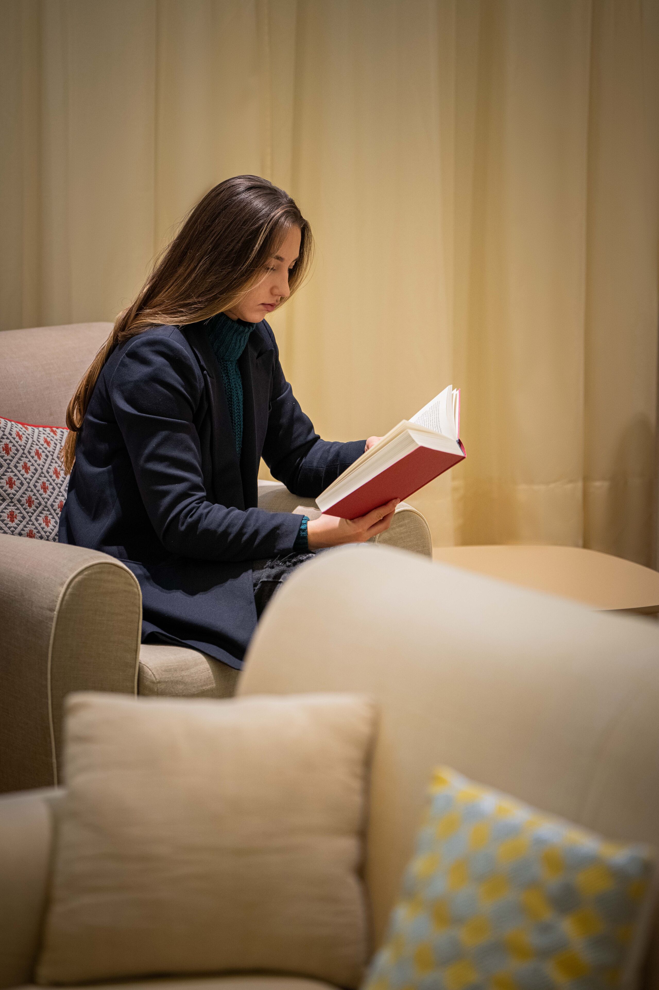 Eine Person sitzt auf einem beige gefärbten Sofa mit gemusterten Kissen und liest ein Buch.