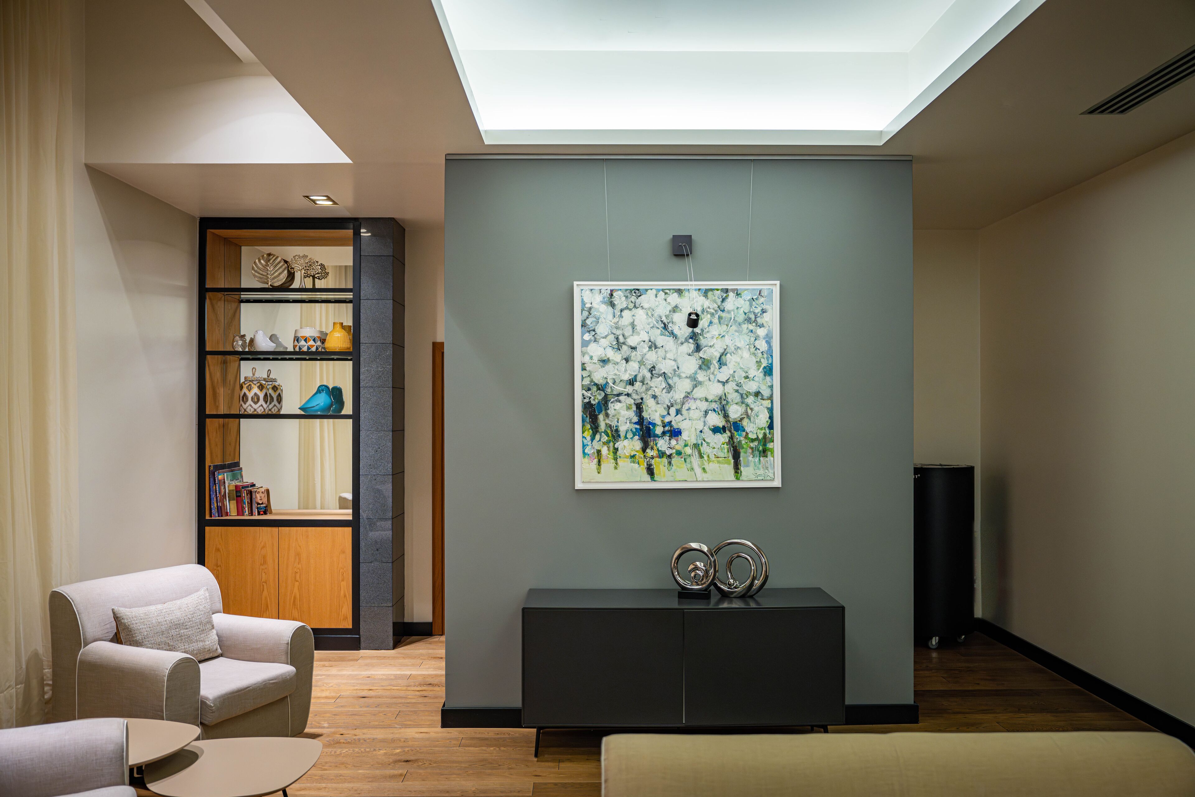 A modern living room with a skylight, a bookshelf, a console table with decorative items, and a large abstract painting on the wall.