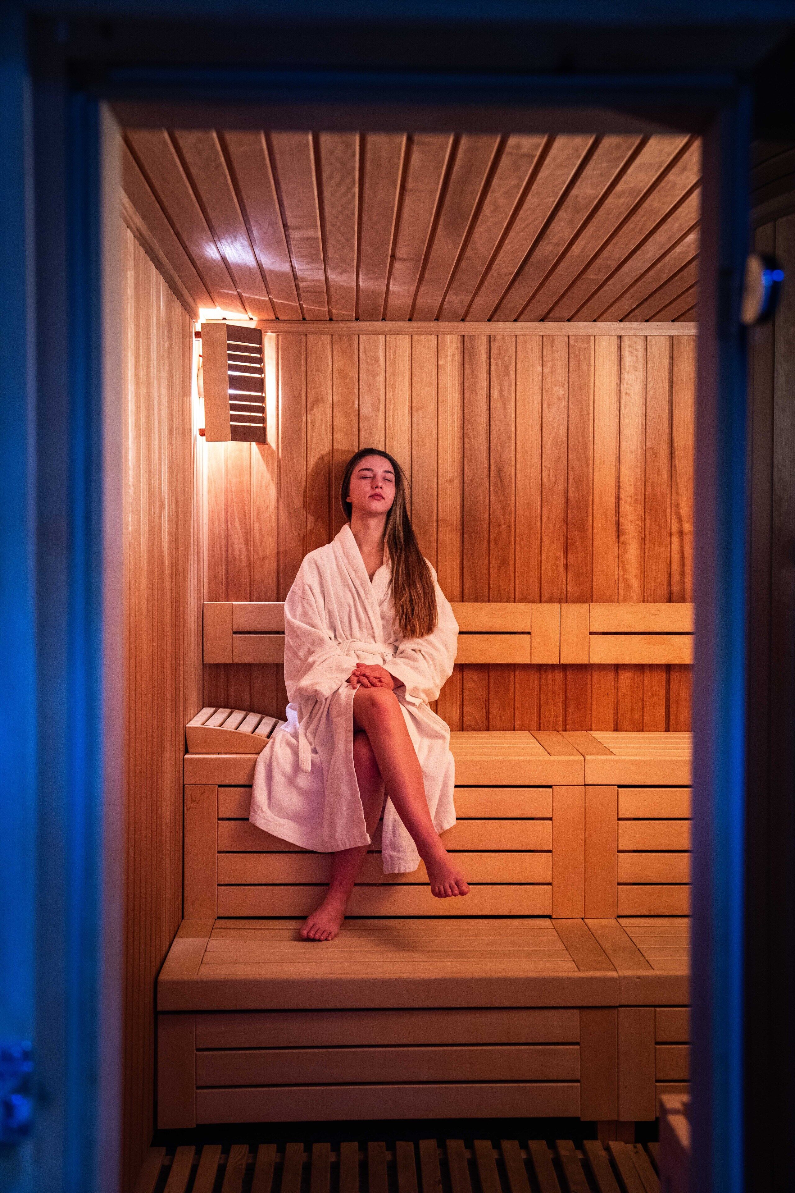 Una persona sentada en una sauna de madera con un banco y techo inclinado.