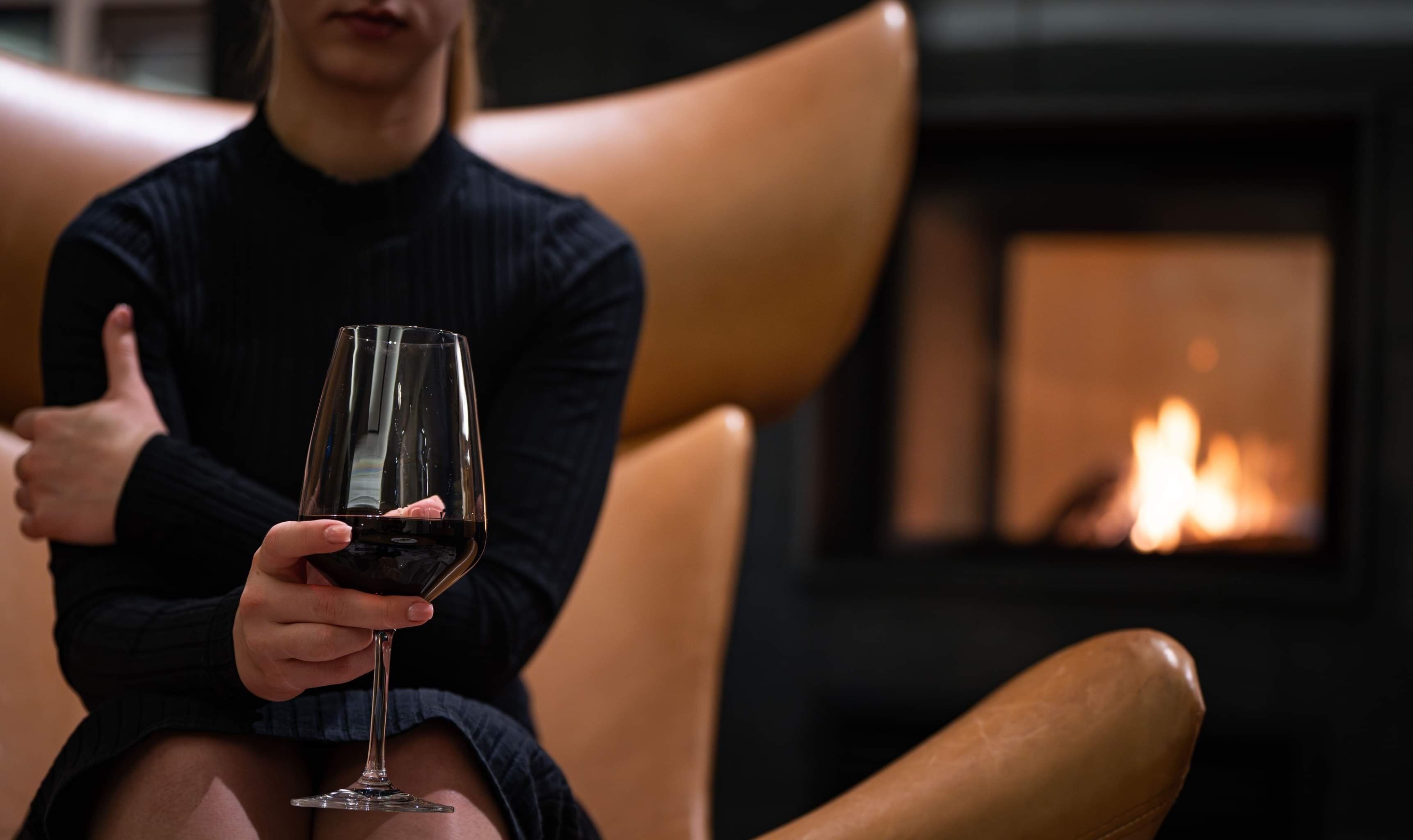 A person sitting on a leather chair holding a wine glass.