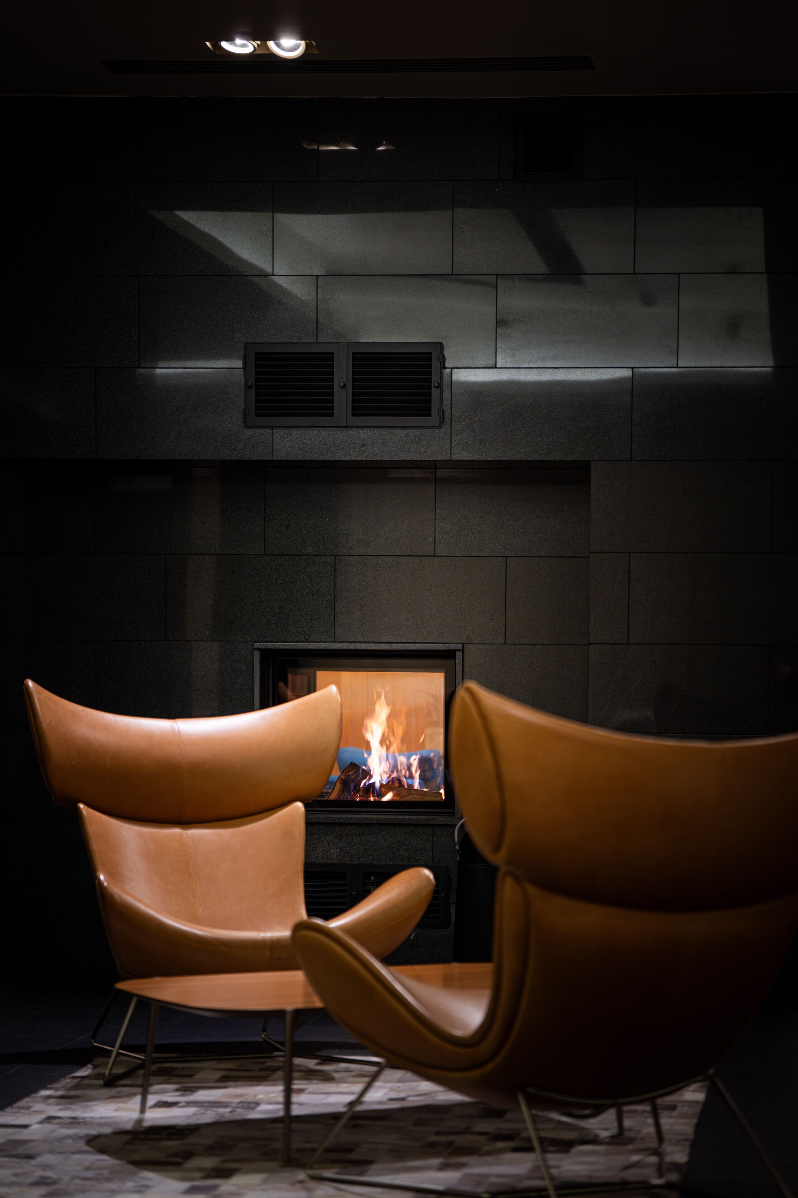 Ein modernes Interieur mit Kamin, zwei Ledersesseln und einem gemusterten Boden.