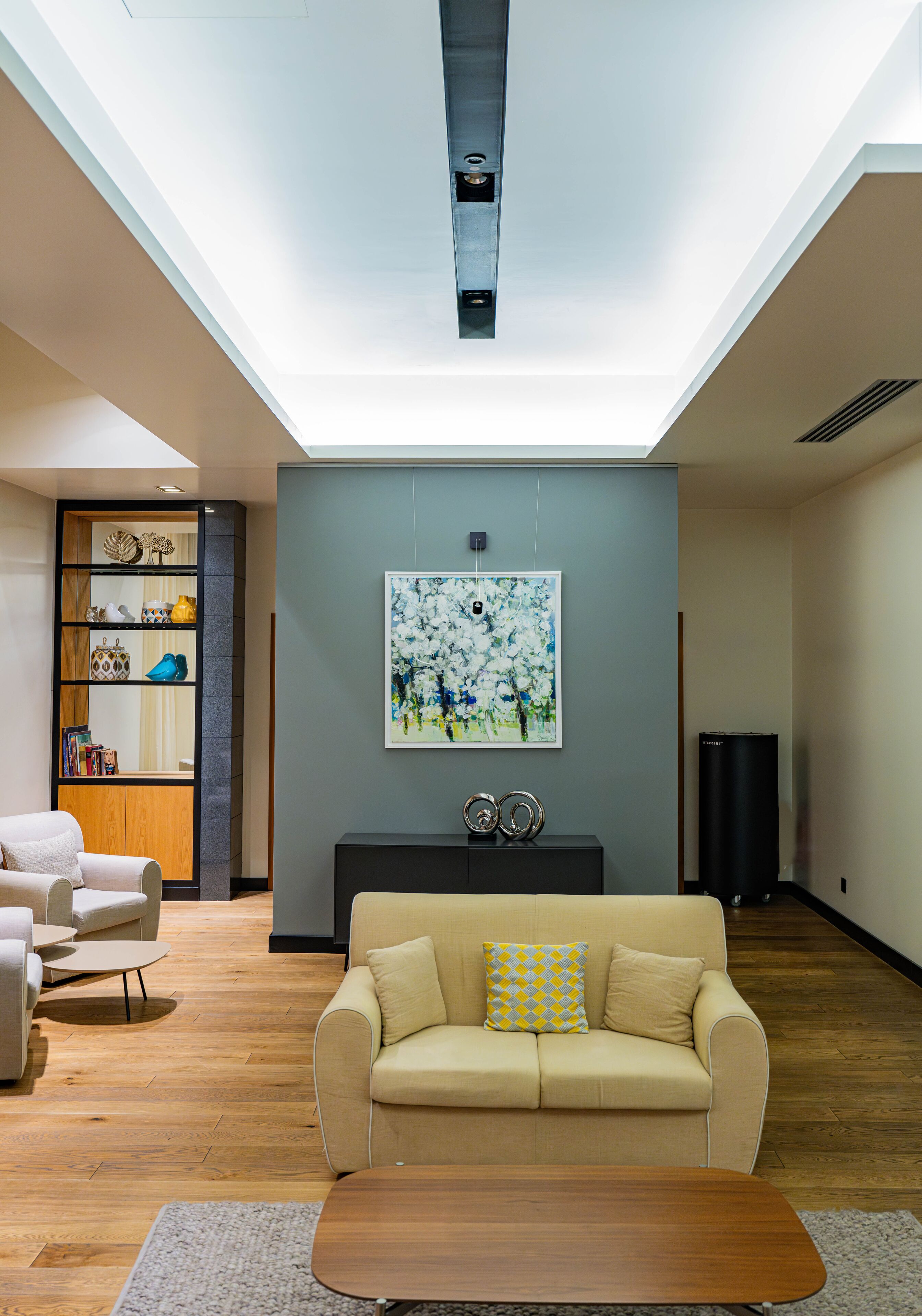 A modern living room with a beige sofa, a wooden coffee table, and a bookshelf.