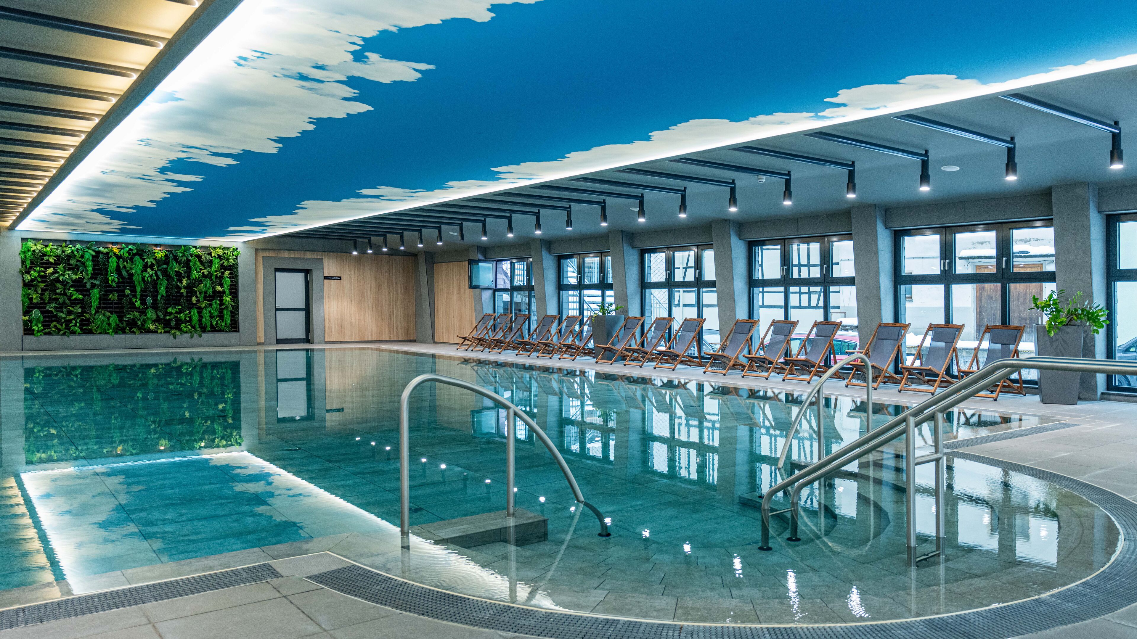 An indoor swimming pool with clear water, surrounded by lounge chairs and large windows.