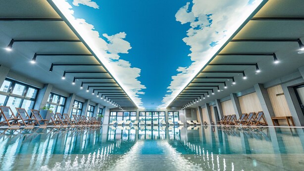Una piscina interior con cielos rasos simulados, ventanas amplias y zonas iluminadas por el sol.