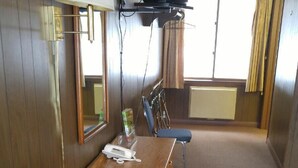 Habitación de hotel con una cama de madera, un escritorio con teléfono, televisor montado en la pared y una ventana con cortinas.