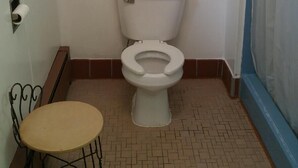 Un baño con inodoro, una mesita pequeña y una cortina de ducha.