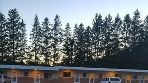 Un motel con varias habitaciones, un estacionamiento y un área verde al frente.