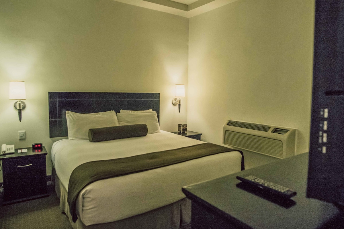 A hotel room with a bed, bedside lamps, a nightstand, a heater, and a remote control.