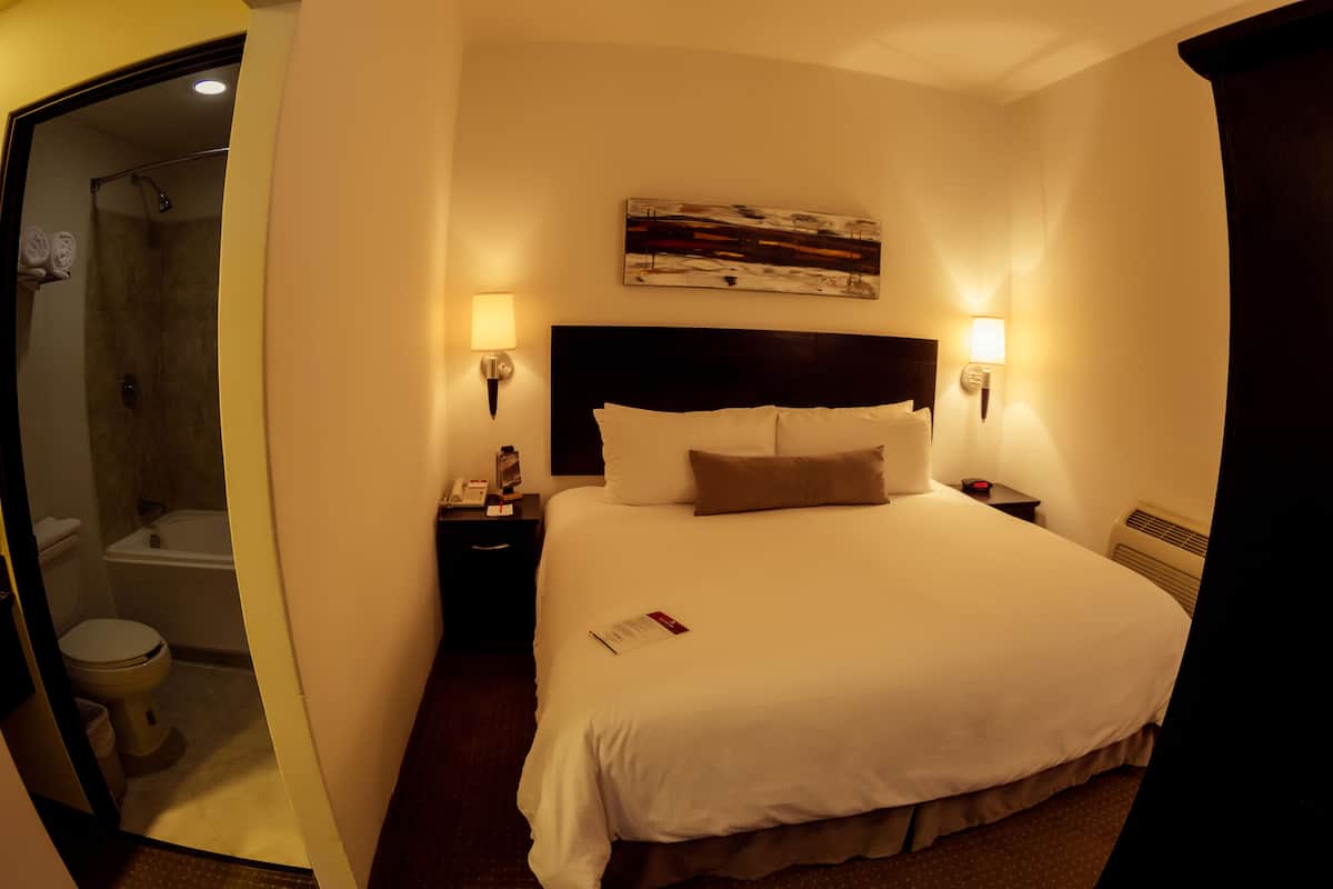 A hotel room with a large bed, two bedside lamps, a painting above the bed, a shower, and a toilet.