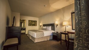 A hotel room with a bed, bedside tables, a desk, a chair, a dresser, and a mirror.